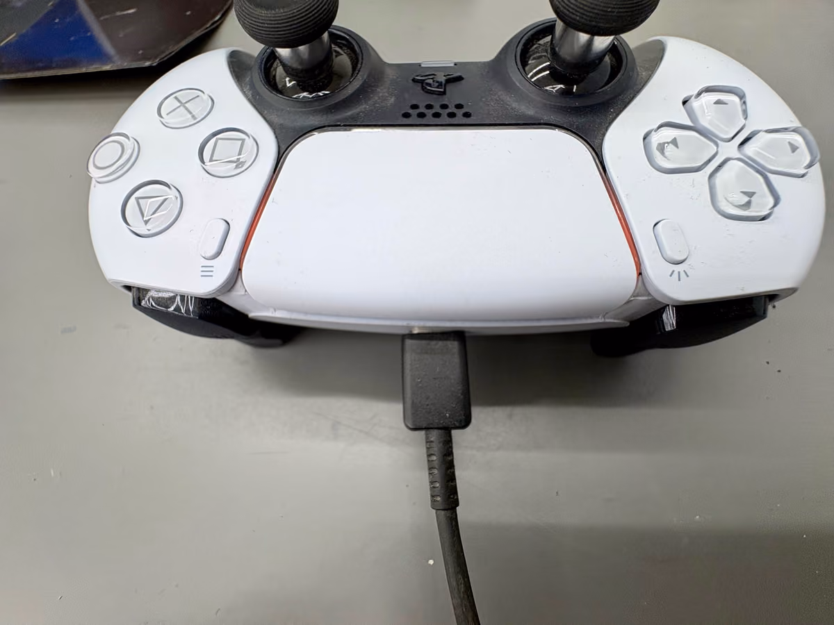 DualSense-controller met USB-C kabel aangesloten, oranje laadlampje zichtbaar