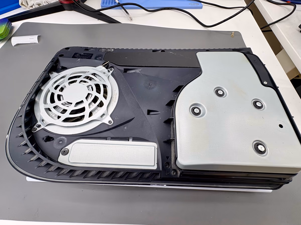 Geopende PS5 op de werkbank met de bevestigingsschroeven van het Blu-ray-station in beeld