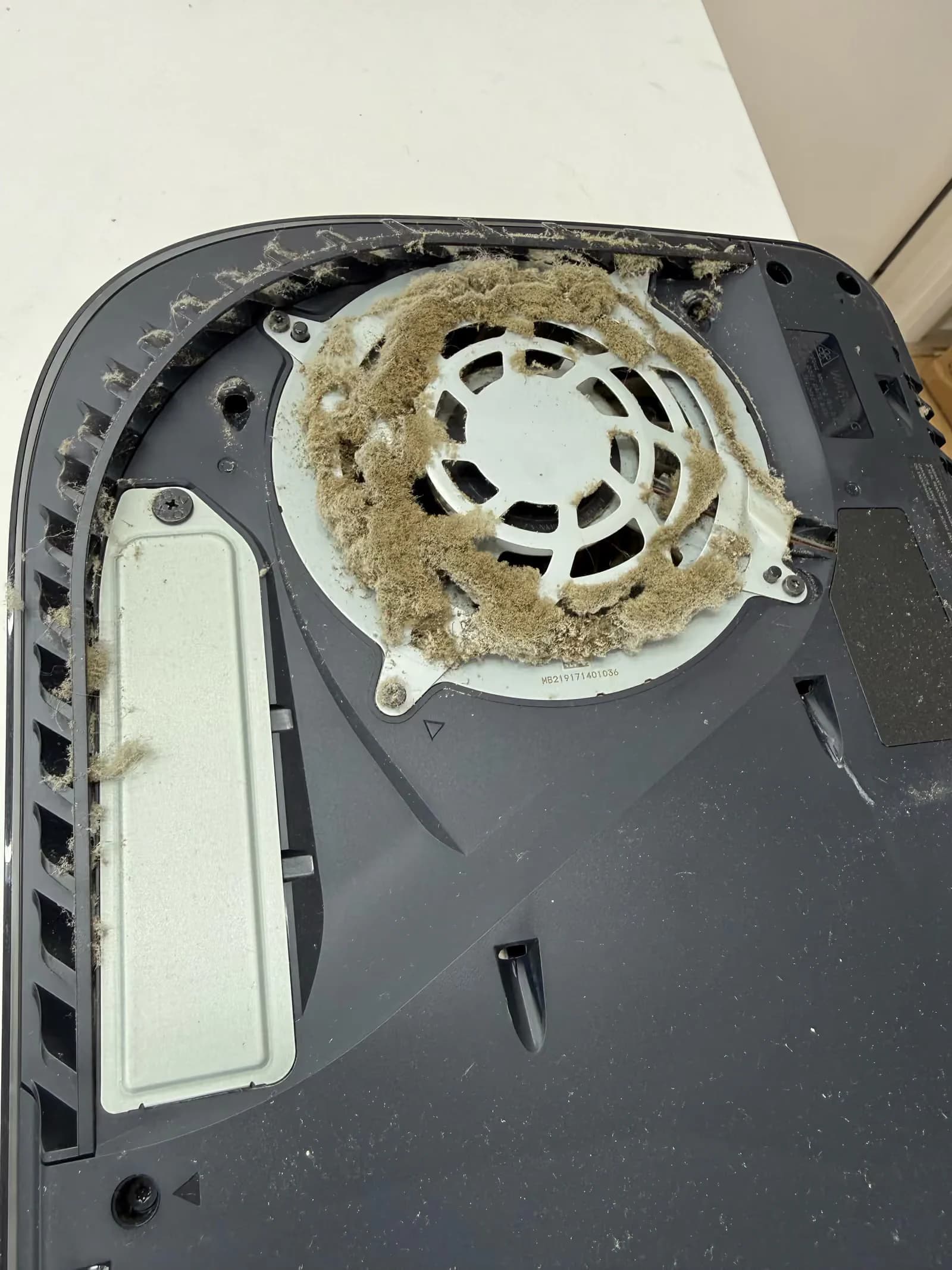 Geopende PS5 met een dikke laag stof en pluis rond de ventilator en in de luchtsleuven